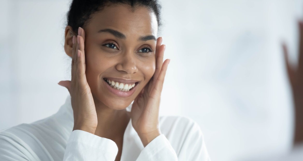 Mulher sorri ao cuidar de sua pele facial para promover a renovação celular e ter uma pele saudável e lisa